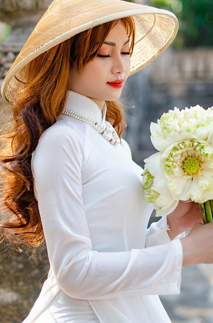 Asian Woman Wearing Tan Hat and White Clothing Holding Beautiful Flowers